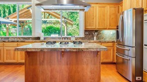 A modern kitchen with wooden cabinets, a central island with a gas range, and a stainless steel refrigerator. - Wine Country Harvest Vacation Home (Santa Rosa)