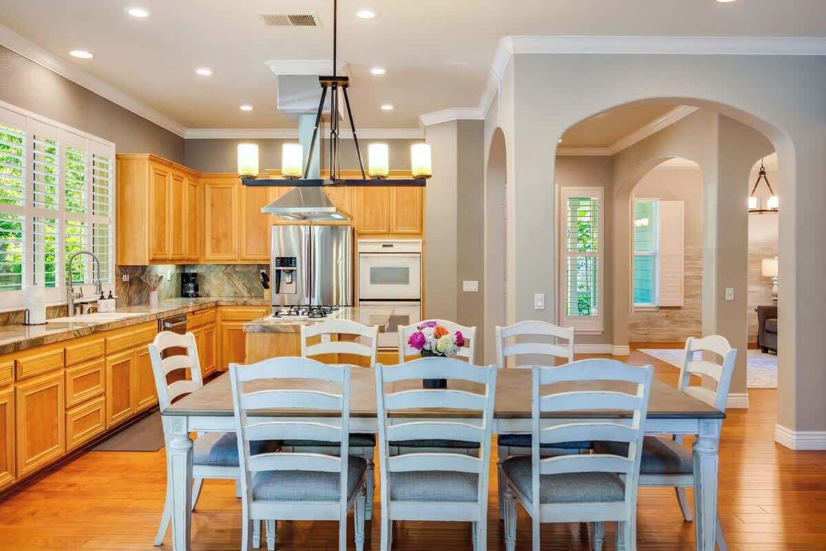 A modern kitchen with wooden cabinets, a central island, and a dining area with white chairs.