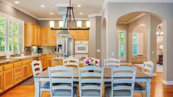 A modern kitchen with wooden cabinets, a central island, and a dining area with white chairs.