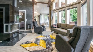 Un vaste espace de vie doté d’une cheminée, de meubles modernes et de grandes fenêtres offrant une vue sur l’extérieur.