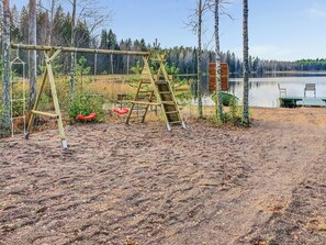 A playground with swings and a ladder, surrounded by trees and a body of water.