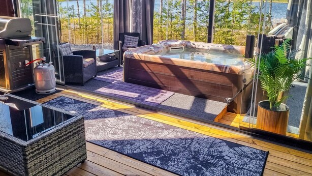 Un espace extérieur abrité par des parois de verre, comprenant un jacuzzi, des sièges et un barbecue.