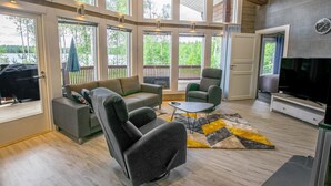 Un salon spacieux doté de grandes fenêtres, d’un canapé, d’un fauteuil, d’une table basse et d’un téléviseur à écran plat.