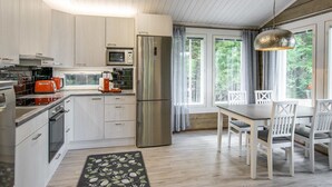 Une cuisine moderne dotée d’appareils électroménagers en acier inoxydable, un coin repas avec une table et des chaises, et de grandes fenêtres offrant une vue sur l’extérieur.