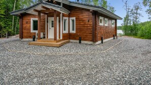 Une cabane en bois dotée d’un porche, d’une allée en gravier et bordée par une forêt.