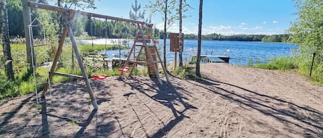 A sandy beach with a swing set and a dock extending into a lake.