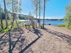 A sandy beach with a swing set and a dock extending into a lake. - Nummentähti by Interhome (Tammela)