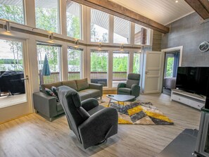 A spacious living room with a large window, a sofa, a chair, a coffee table, and a television. - Nummentähti by Interhome (Tammela)