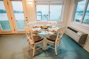 A dining area with a table set for four, white chairs, and a view of a marina through large windows. - Waterfront • Hot Tub • Beach • Dock • Kayaks (White Stone)