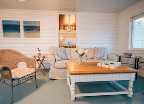 A living room with a wicker chair, a sofa, a coffee table, and a small side table with books.