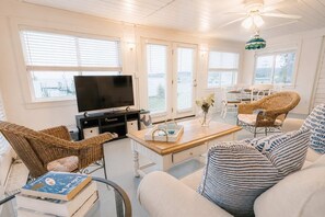 A living room with a television, wicker furniture, a dining area with chairs, and a ceiling fan. - Waterfront • Hot Tub • Beach • Dock • Kayaks (White Stone)