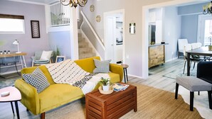Un salon avec un canapé jaune, une table basse en bois et un escalier menant à une mezzanine.