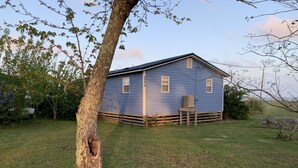Uma casa térrea com fachada azul, um pequeno alpendre com uma cadeira e um gramado.