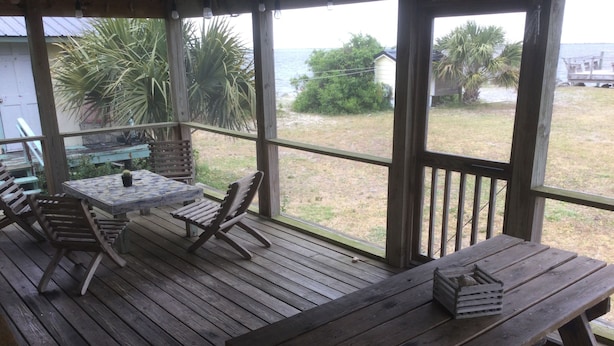 Um deck de madeira com mesa e cadeiras, com vista para uma área gramada e o oceano.