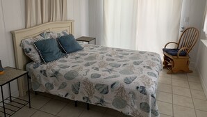 Um quarto com uma cama, uma cadeira de madeira, uma mesa pequena e cortinas.