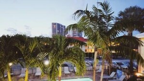Une piscine entourée de palmiers et de chaises longues, avec une vue sur la ville en arrière-plan.