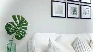 Un canapé blanc avec des coussins à rayures, une plante verte dans un vase en verre et trois tableaux encadrés accrochés au mur.