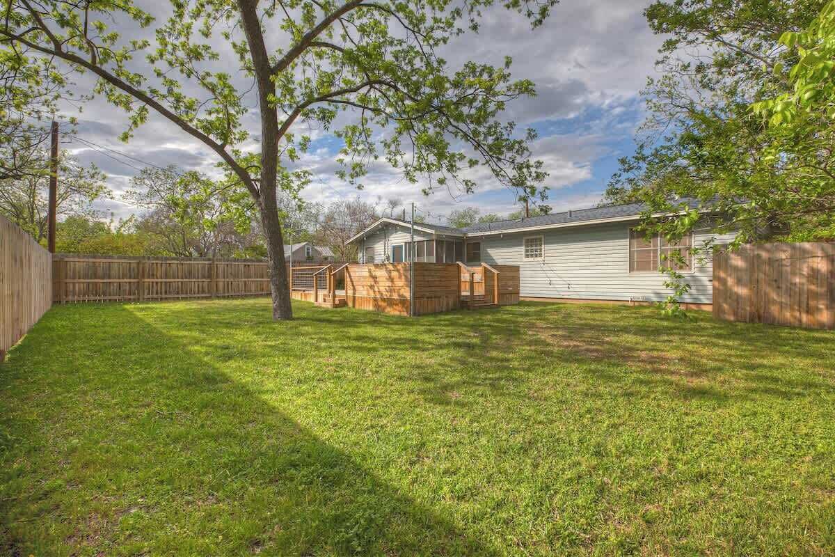 Un jardin avec une cabane en bois, un espace délimité par une clôture et une maison dotée d’un toit en pente.