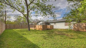 Un patio trasero con una casita de juegos de madera, un área cercada y una casa con techo inclinado.
