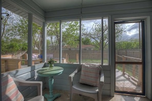 Um alpendre coberto com mesa e cadeiras, janelas amplas e vista para o quintal.