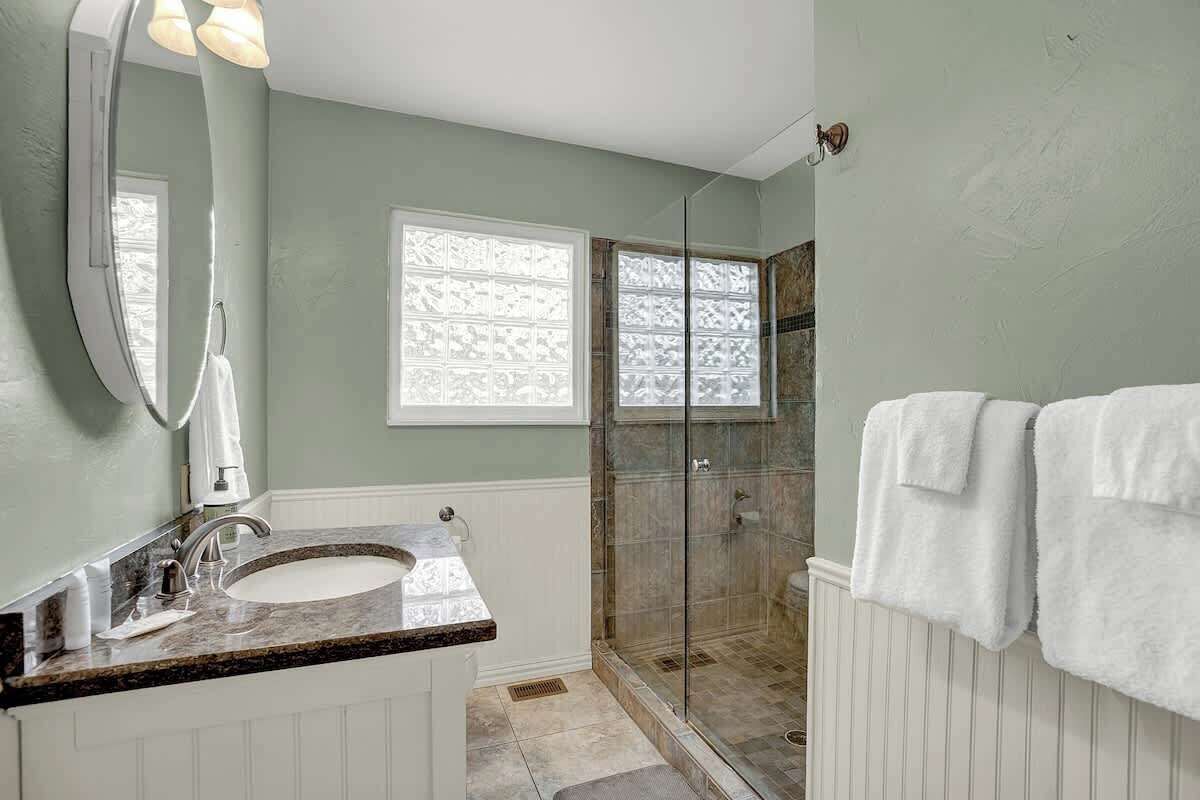 Une salle de bain dotée d’un double lavabo, d’une douche à parois de verre et d’une fenêtre avec des panneaux en verre dépoli.