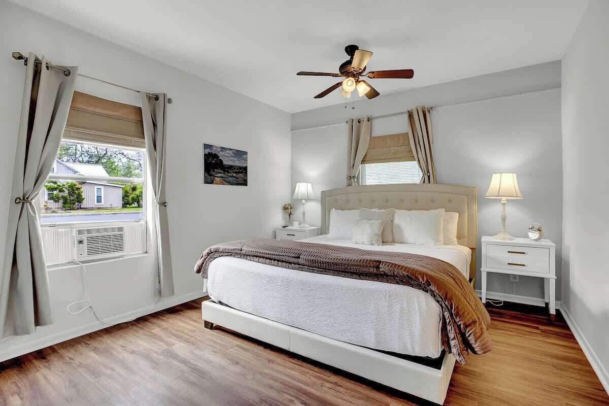 Ein Schlafzimmer mit Bett, Nachttischen, Deckenventilator und einem Fenster mit Vorhängen.