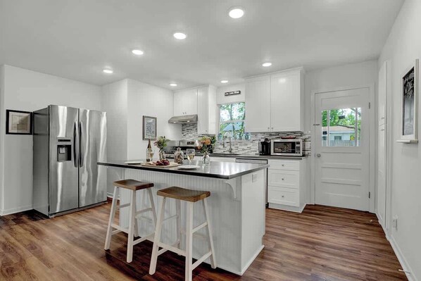 A modern kitchen with white cabinets, stainless steel appliances, and a wooden island with stools.