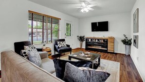 Una sala de estar con un sofá, sillones, una mesa de centro y un televisor montado en la pared.