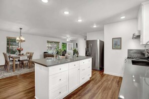 A modern kitchen with white cabinetry, a large island, and a stainless steel refrigerator. - Bluebonnet House-Deck w/fire table (Fredericksburg)