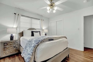 A bedroom with a bed, nightstands, a ceiling fan, and a door.
