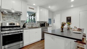 Una cocina moderna con gabinetes blancos, electrodomésticos de acero inoxidable y una isla central.