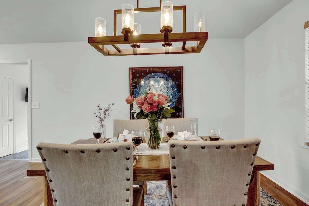 Un espace repas comprenant une table en bois, des chaises rembourrées, un lustre et un élément décoratif mural.