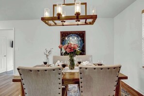 Un comedor con una mesa de madera, sillas tapizadas, una araña y un adorno en la pared.