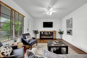 Ein Wohnzimmer mit Kamin, einem an der Wand befestigten Fernseher und einem Deckenventilator.