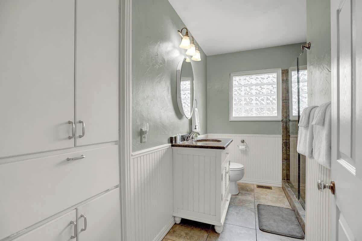 Un baño con tocador blanco, lavamanos, espejo, inodoro y zona de ducha.