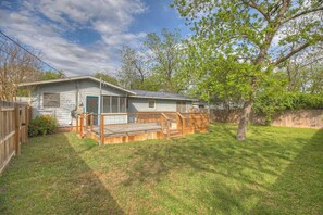 A single-story house with a front porch, a fenced yard, and a large tree. - Bluebonnet House-Deck w/fire table (Fredericksburg)