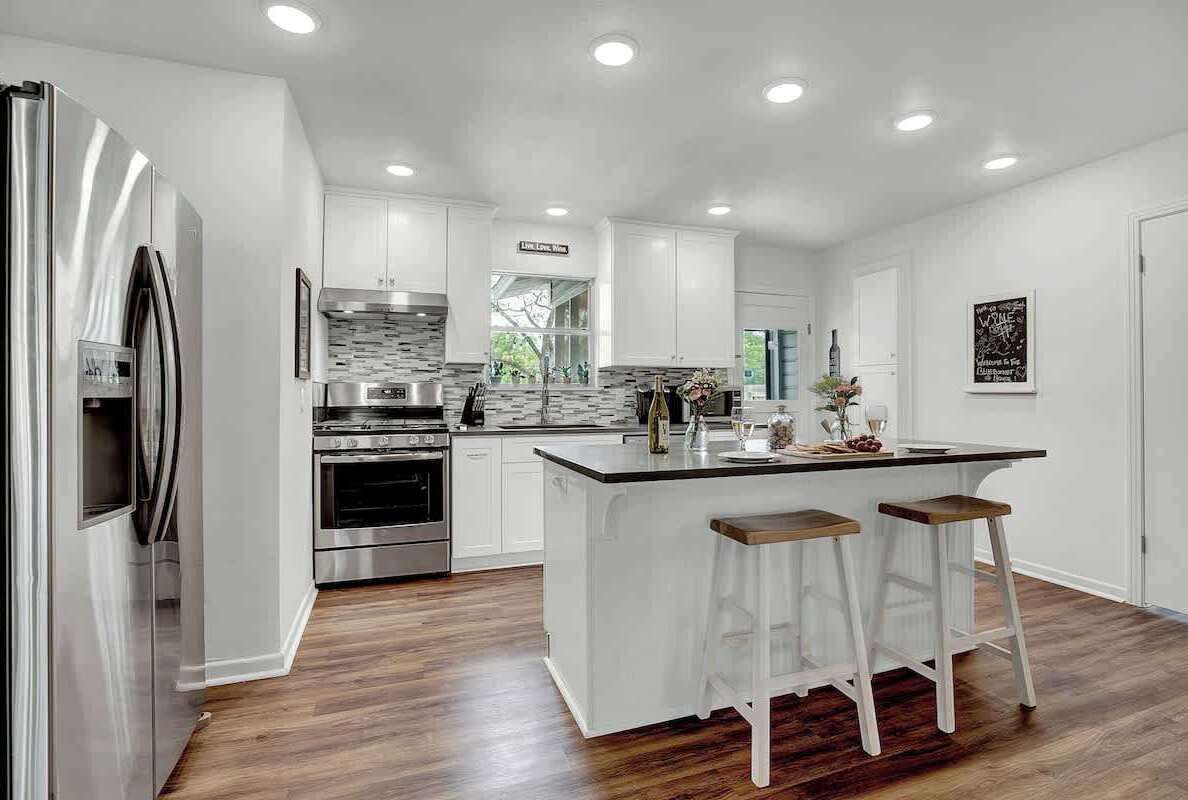Una cocina moderna con armarios blancos, electrodomésticos de acero inoxidable y una isla central con taburetes.