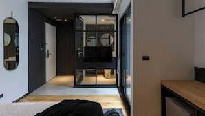 Une chambre moderne avec un lit, un plancher en bois, une télévision et une porte en verre donnant sur une salle de bain.