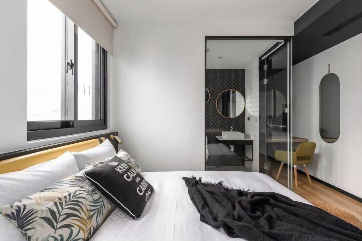 Una habitación de hotel moderna con una cama, una ventana, un espejo y un baño visible a través de un cristal.