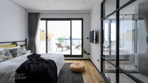 Une chambre d’hôtel moderne équipée d’un lit, d’une grande fenêtre, d’un balcon et d’une télévision.