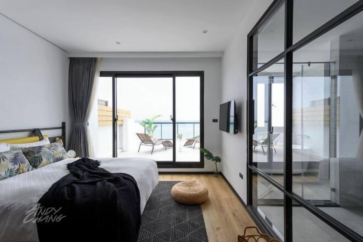 Una habitación de hotel moderna con cama, ventana grande, balcón y televisor.