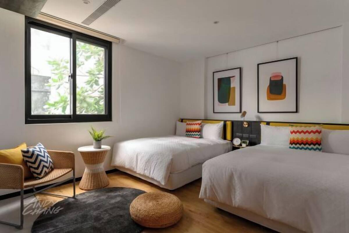 Una habitación de hotel moderna con dos camas, una mesita redonda pequeña, una silla y un ventanal grande.