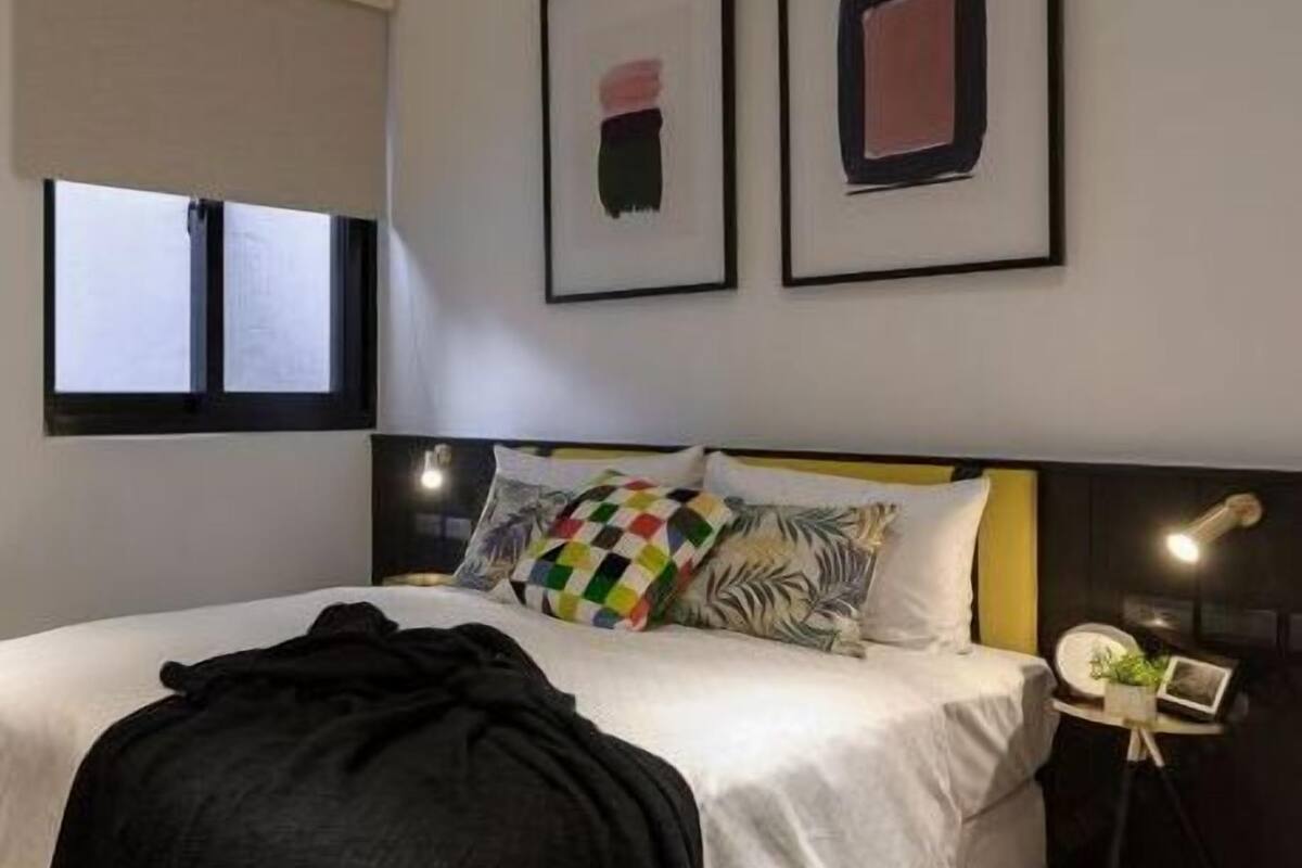 Un dormitorio moderno con una cama, una mesita de noche, una lámpara y dos cuadros enmarcados en la pared.