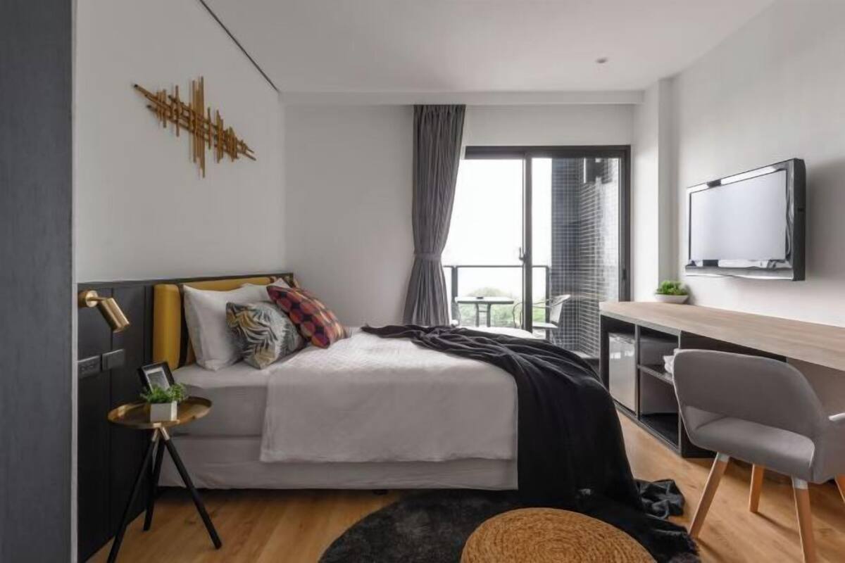 Un dormitorio moderno con cama, mesita de noche, televisor y vistas al exterior.