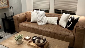 Una sala de estar moderna con un sofá de cuero marrón, una mesa de centro de madera y un cuadro abstracto grande en la pared.