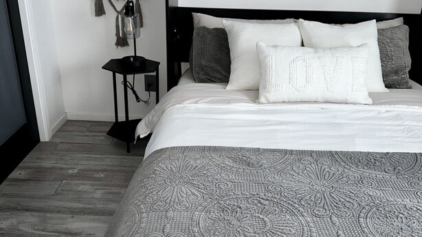 Un dormitorio ordenado con una cama grande, una mesita de noche, un atrapasueños colgado en la pared y una manta decorativa.
