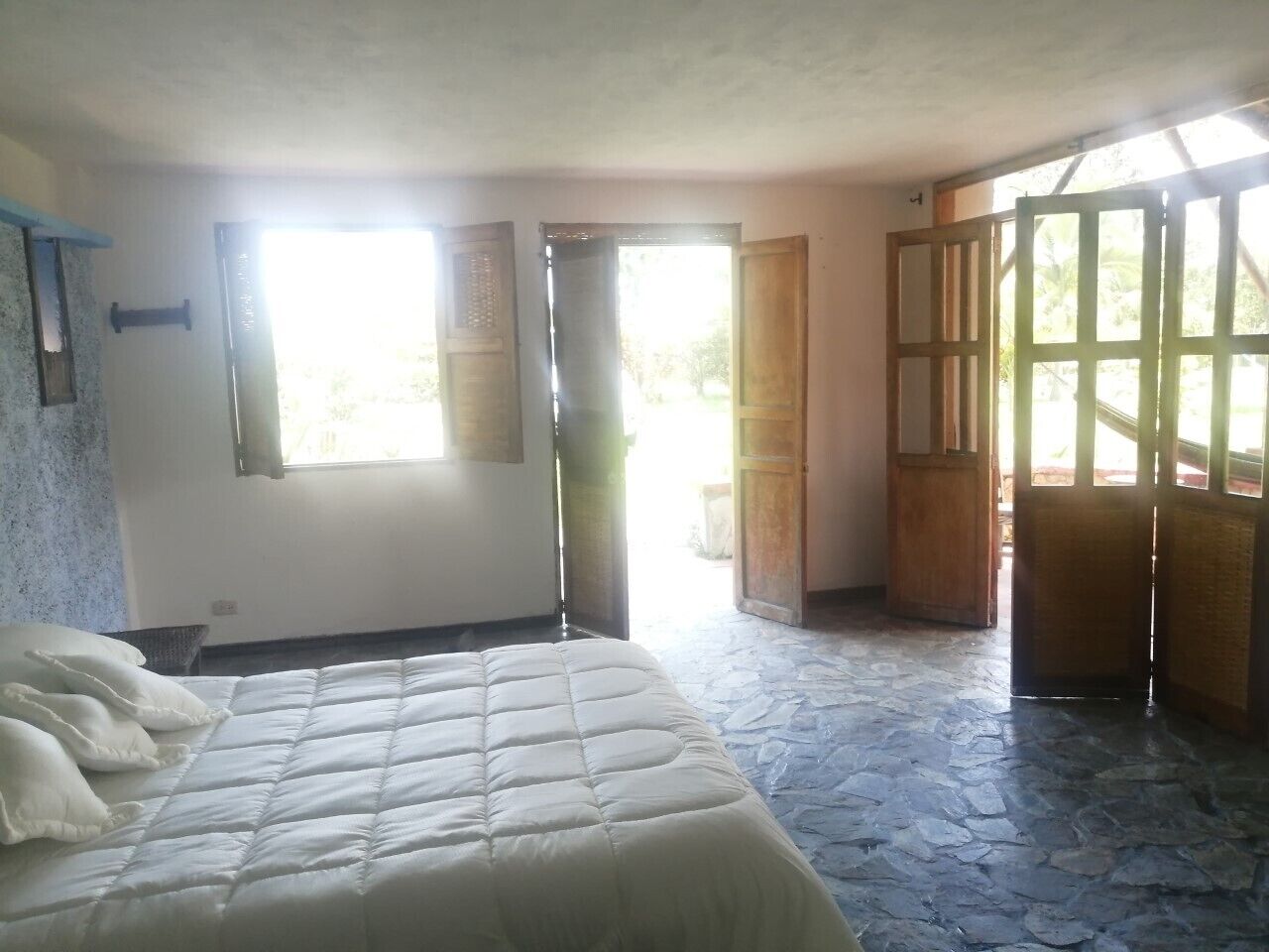 Quarto com cama, janela e porta que dá para área externa.