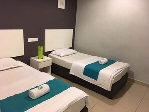 Camera d'albergo con due letti singoli, ciascuno con materasso bianco e copripiumino verde acqua. Si notano due comodini bianchi, su uno dei quali c'è una lampada verde.