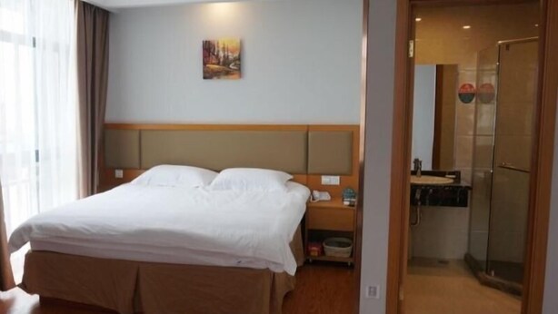 A hotel room with a bed, a nightstand, a painting on the wall, and a bathroom visible through an open door. - Greentree Inn Henan Xinyang Shangcheng County Huangbaishan Road Times Shopping Mall Express Hotel (Xinyang)