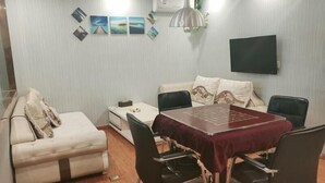 A compact living space with a dining table, chairs, a sofa, and a TV mounted on the wall. - Greentree Inn Henan Xinyang Shangcheng County Huangbaishan Road Times Shopping Mall Express Hotel (Xinyang)